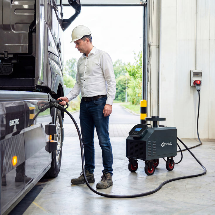 Technician in a hard hat DC fast charging an electric truck in a workshop